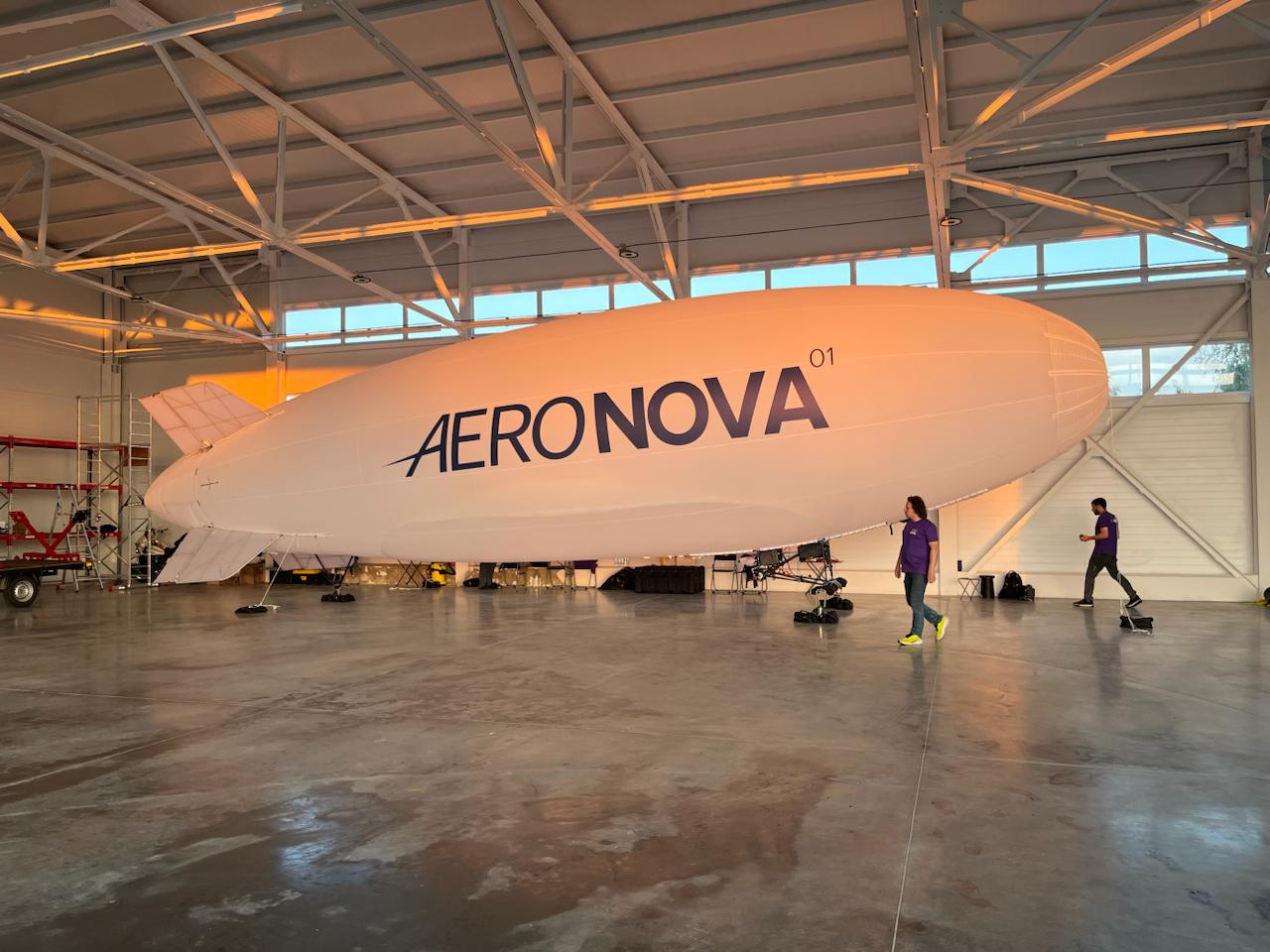NOVA-01 · 130 m³ · in the AERONOVA hangar at sunset · scale reference with engineers